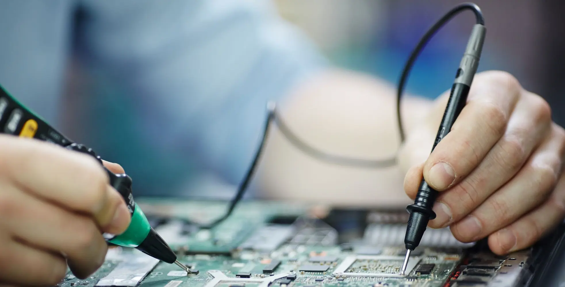 Testen der elektrischen Spannung auf der Platine eines zerlegten Laptops mit einem Multimeter auf dem Tisch in der Werkstatt