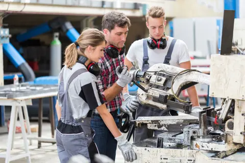 Ausbilder und zwei Azubis bei der Arbeit an einer Maschine